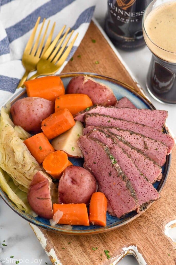 Plate with slices of Instant Pot Corned Beef, carrots, cabbage, and potatoes. Forks and Guinness beer beside.