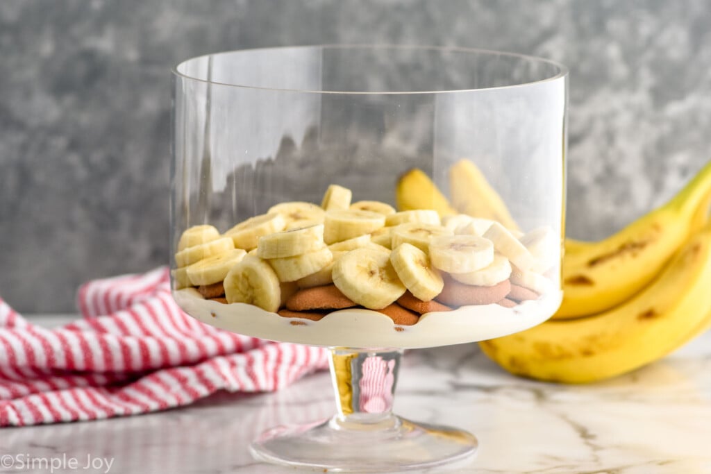 Side view of layered ingredients for Banana Pudding recipe with bananas beside