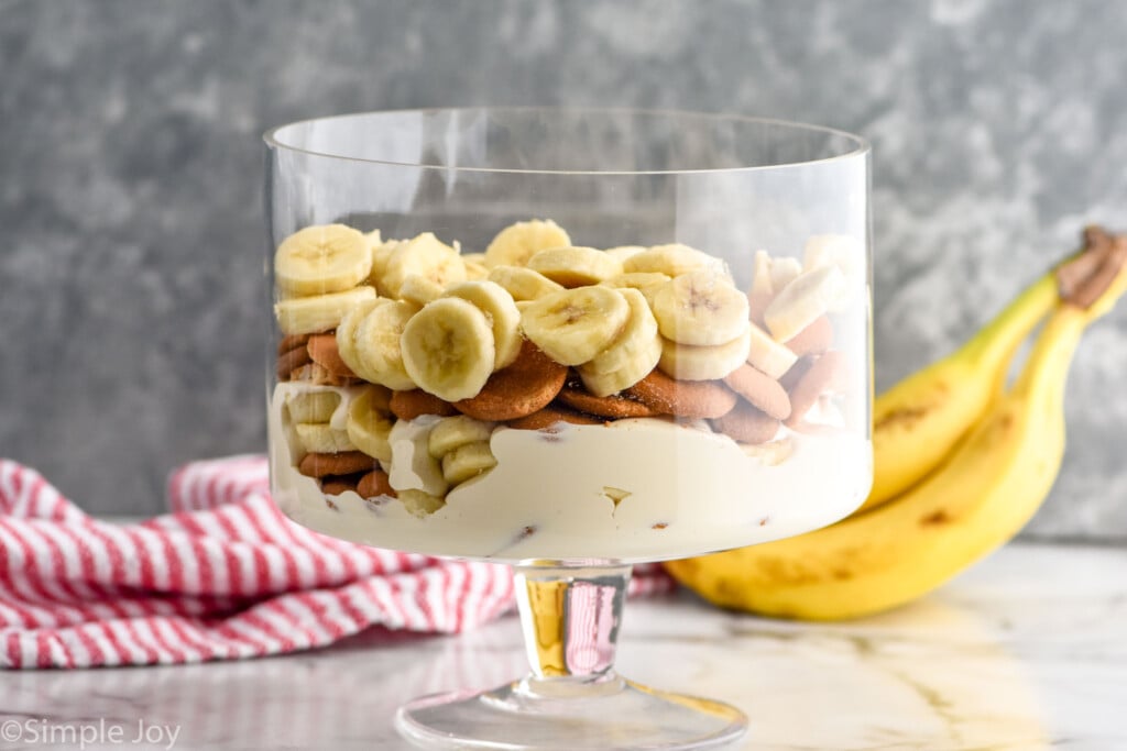 Side view of dish of layered ingredients for Banana Pudding recipe. Bananas beside