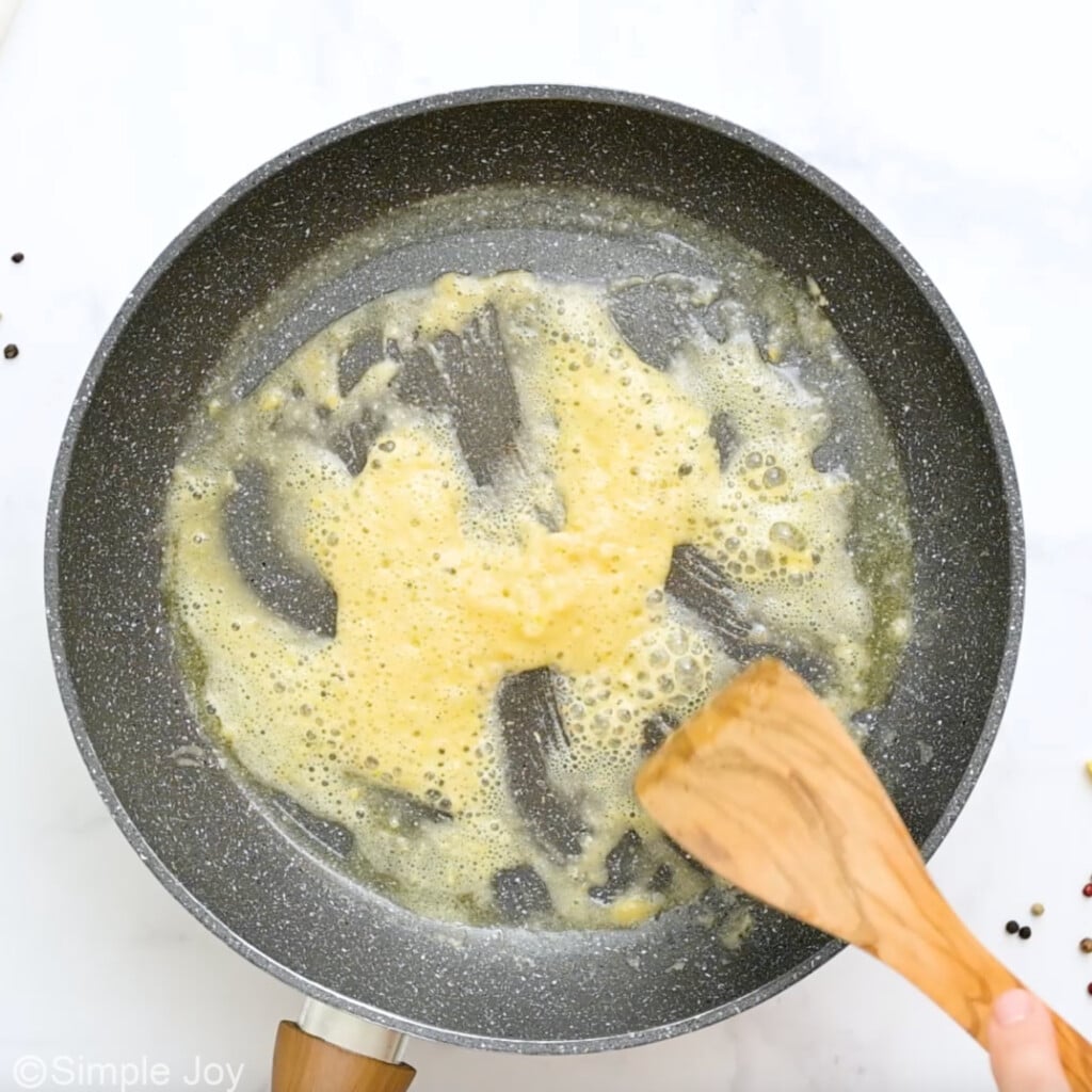 Overhead view of a skillet of butter and garlic cooking for crab pasta recipe with wooden spoon - 6