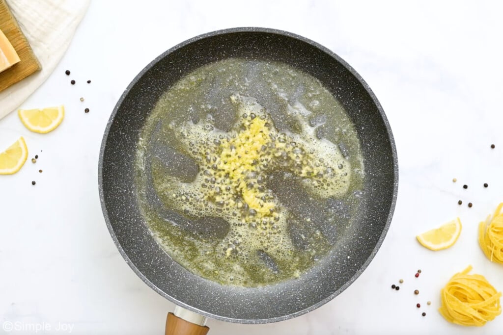 Overhead view of a skillet with butter and garlic cooking for crab pasta recipe. Noodles and lemon slices beside skillet - 5