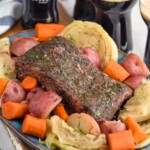 Instant Pot Corned Beef on a platter with cabbage, carrots, and potatoes. Guinness beers beside.