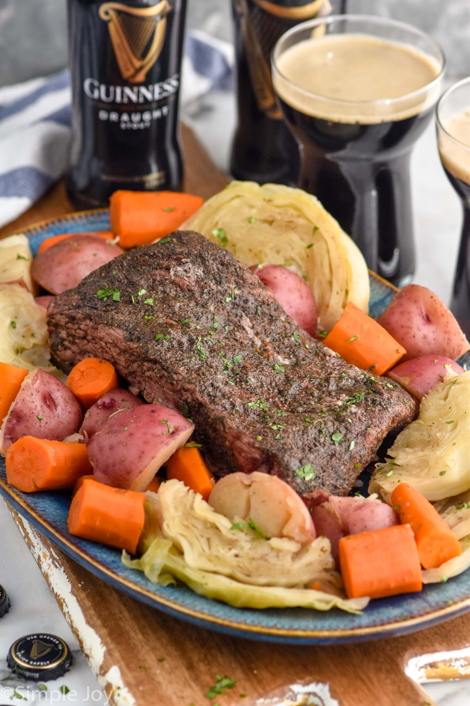 Instant Pot Corned Beef on a platter with cabbage, carrots, and potatoes. Guinness beers beside.