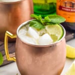 Irish Mule with limes and mint leaves beside, bottles of liqueur behind.