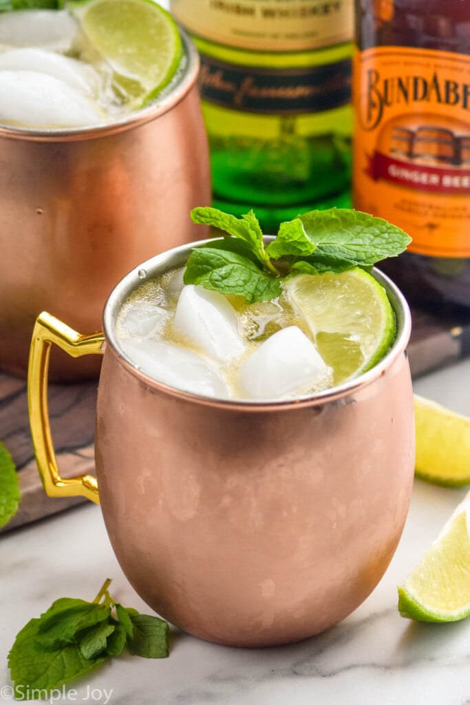 Irish Mule with limes and mint leaves beside, bottles of liqueur behind.