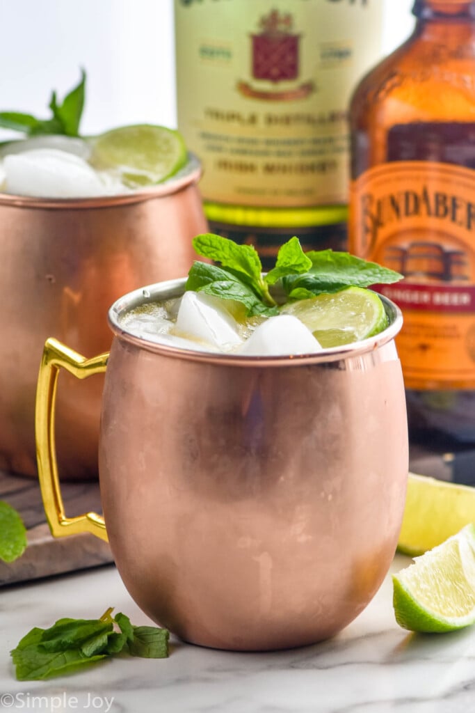 side view of Irish Mule with limes and mint leaves, bottles of liqueur behind
