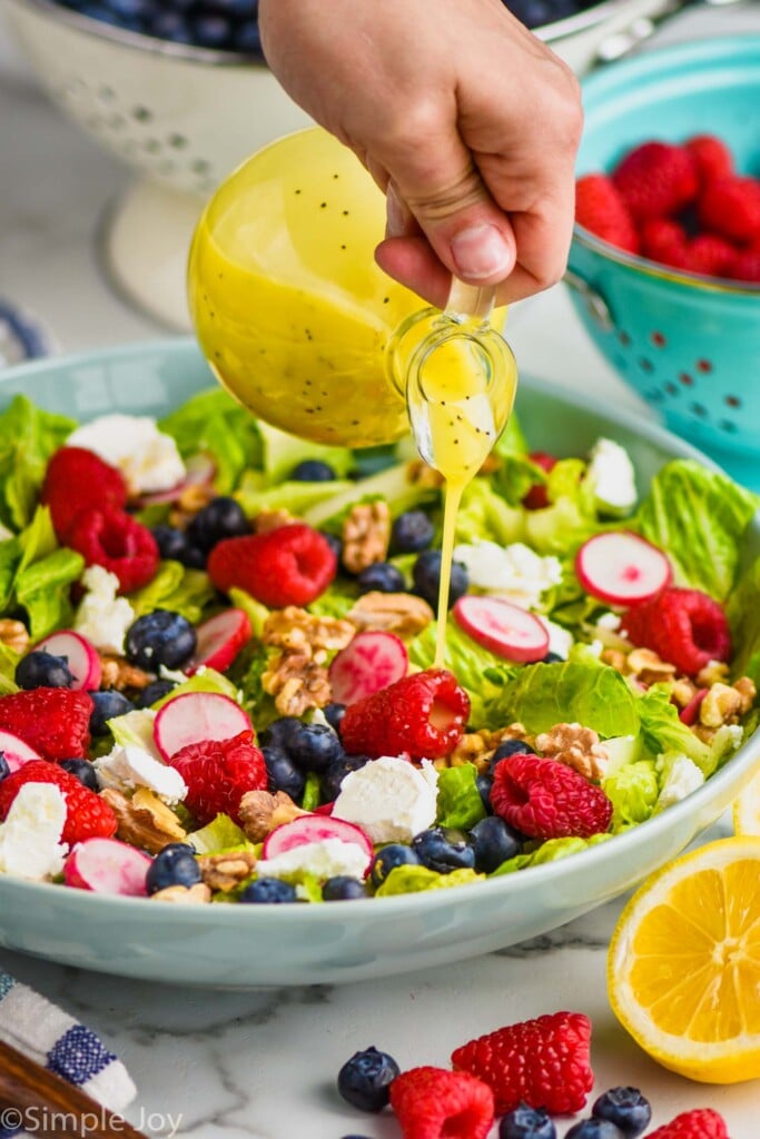 Person's hand pouring Poppy Seed Dressing over salad