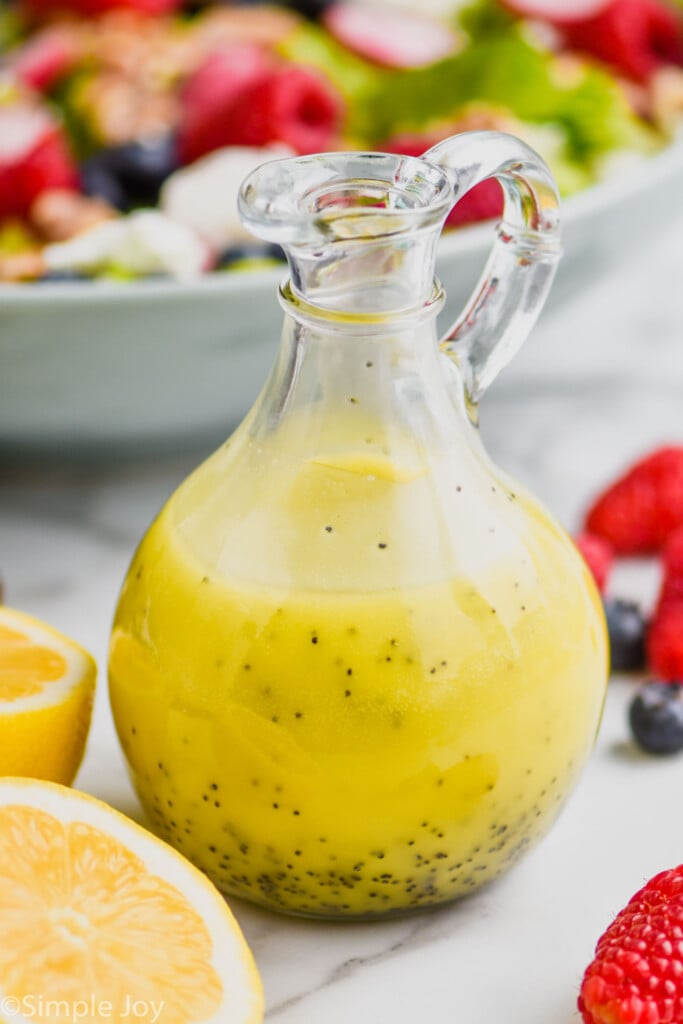 container of Poppy Seed Dressing with sliced lemon, berries, and salad beside