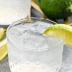 Vodka Gimlet garnished with lime wedge. Lime and another Vodka Gimlet beside. - 8