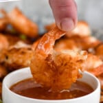Pinterest graphic for Coconut Shrimp recipe. Text says, "the best Coconut Shrimp simplejoy.com." Image shows person's hand dipping Coconut Shrimp into chili sauce.