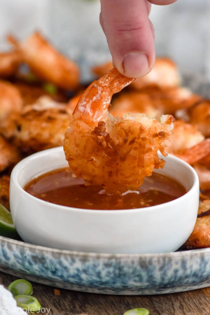Side view of Coconut Shrimp being dipped in chili sauce