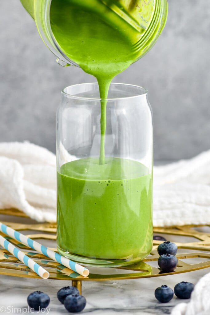 Blender pouring Green Smoothie into a glass with blueberries beside