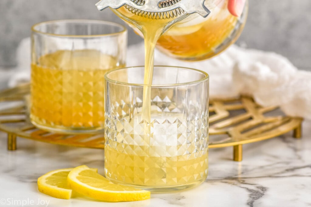 Side view of pitcher of Gold Rush Cocktail recipe being poured into tumbler of with ice.