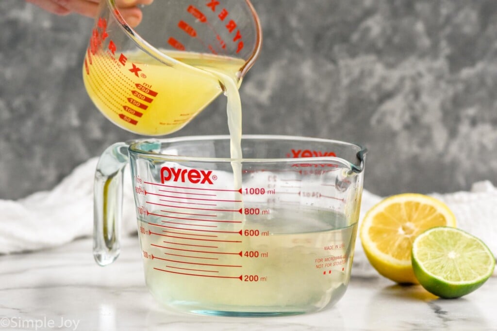 Measuring cups of ingredients for Margarita Mix recipe. Lemon and lime beside.