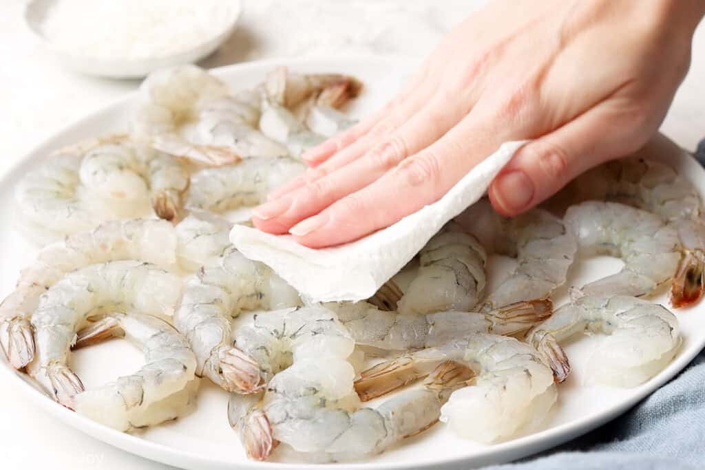 a paper towel patting raw shrimp dry