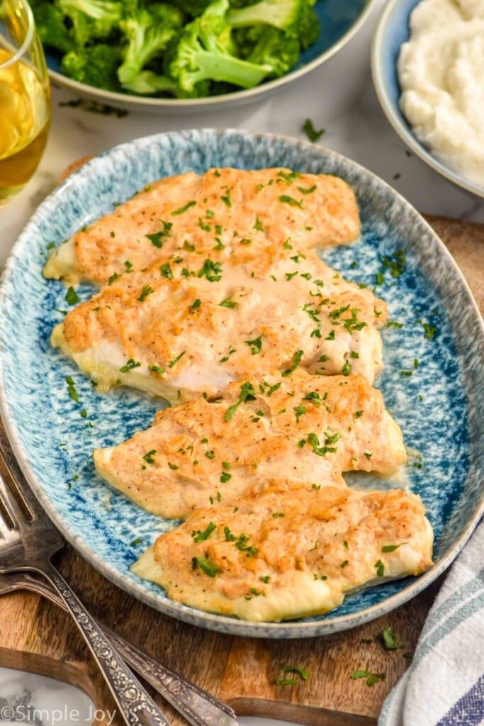 Platter of Melt In Your Mouth Chicken with bowls of broccoli, mashed potatoes, forks, and glass of white wine beside