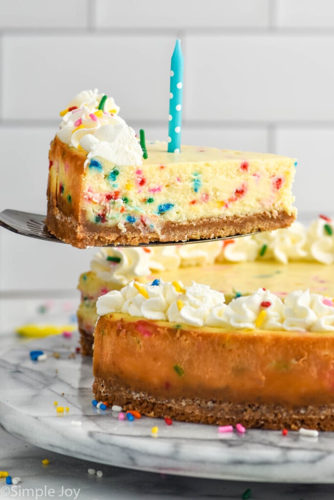 Slice of Birthday Cheesecake being lifted from whole Birthday Cheesecake