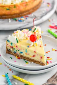 Slice of Birthday Cheesecake with a cherry on top and sprinkles around. Candles and a fork beside the plate