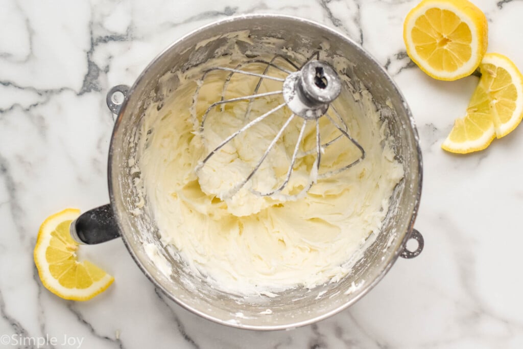 overhead of mixing bowl of Lemon Buttercream Frosting and beaters. Lemon slices sitting beside