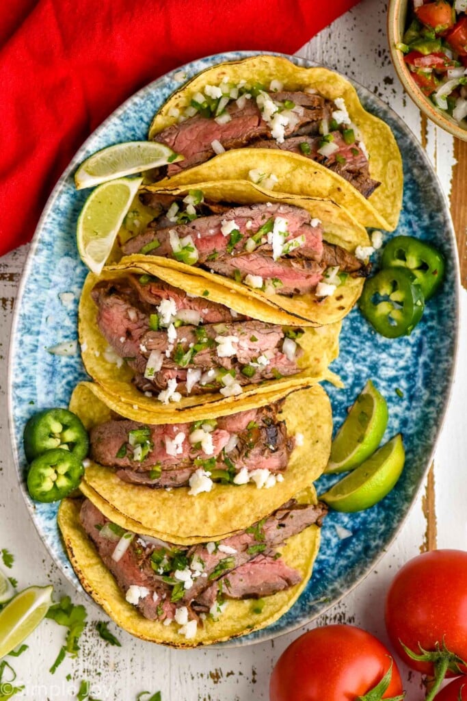 overhead of a plate of carne asada meat in tacos, topped with cojito cheese, onions, and jalapeños