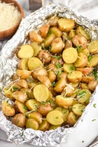grilled potatoes in foil garnished with shredded cheese and parsley