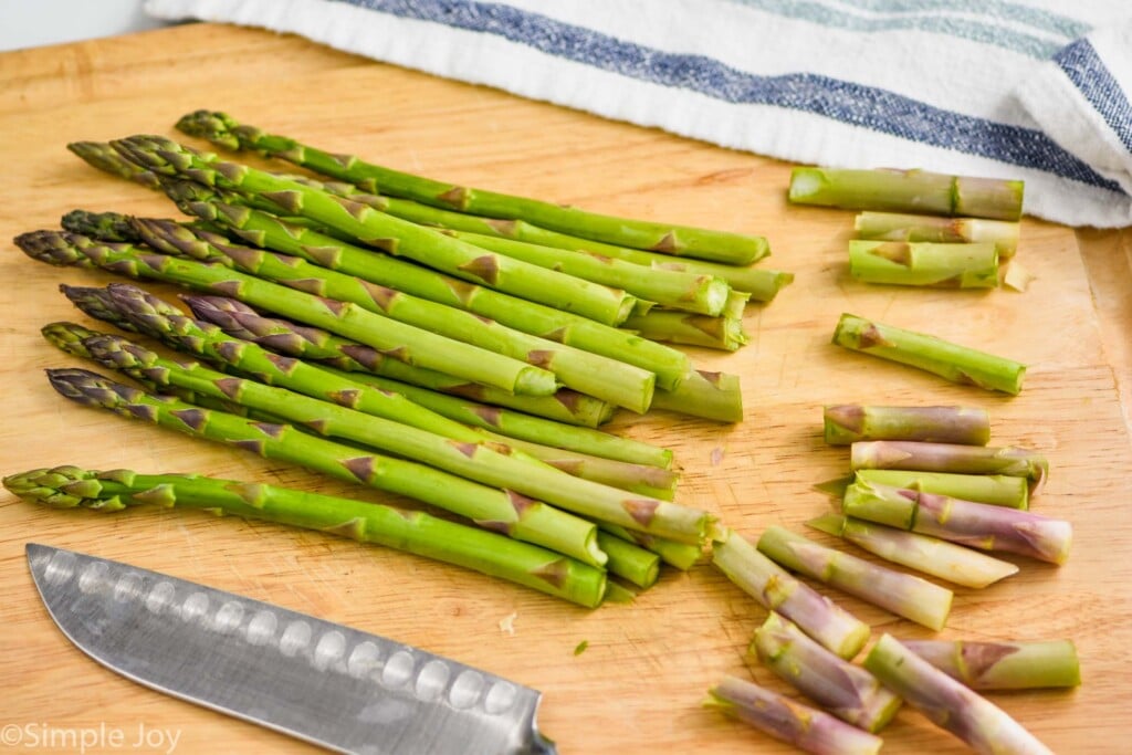 bunch of asparagus on a wood cutting board with woody bottoms snapped off to make oven roasted asparagus