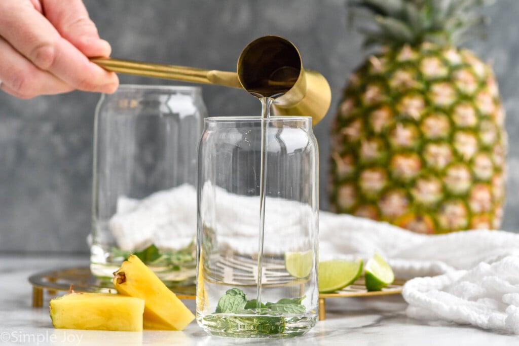 Side view of cocktail jigger of ingredients being poured into glass for Pineapple Mojito recipe.