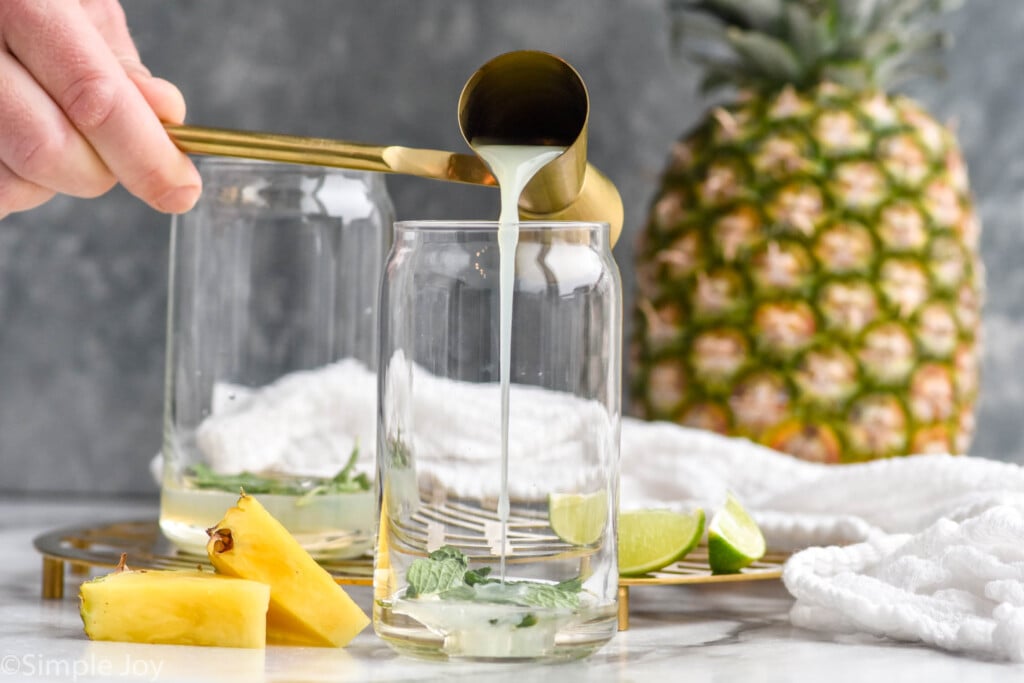 Side view of cocktail jigger being poured into glass of ingredients for Pineapple Mojito recipe.
