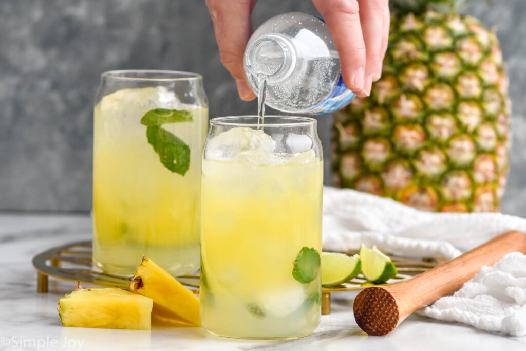 Side view of person's hand pouring club soda into glass for Pineapple Mojito recipe