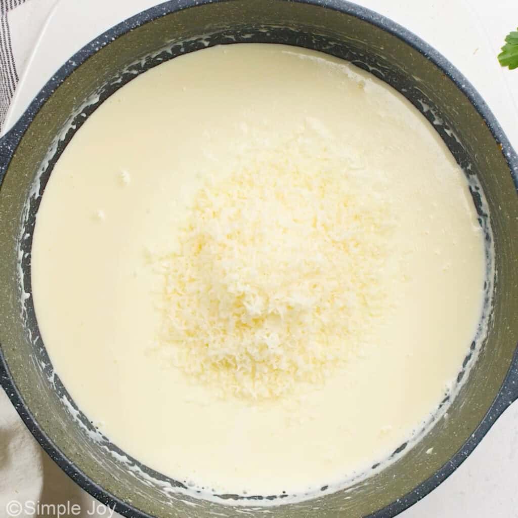adding shredded parmesan to a cream sauce in a skillet