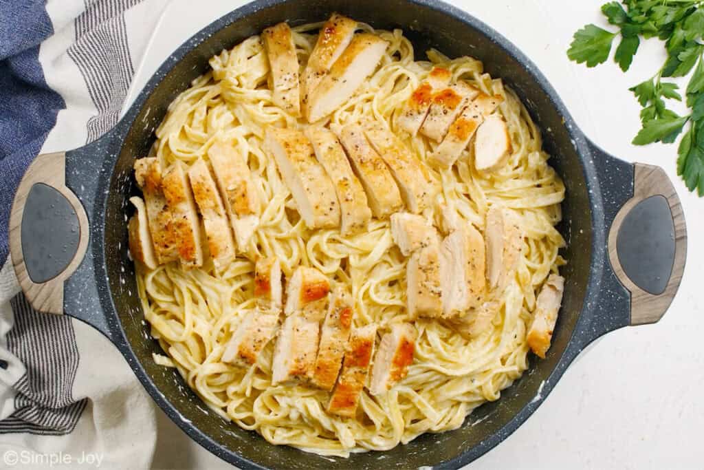 overhead of a skillet with browned chicken and fettuccine Alfredo