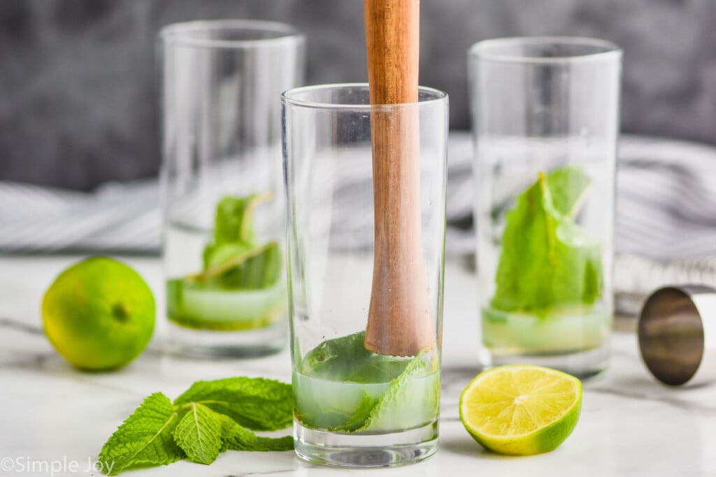 a muddler going into a high ball glass that has lime juice and mint in it