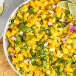 Overhead view of Pineapple Mango Salsa garnished with cilantro and lime wedges, with chips beside - 10