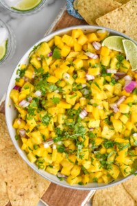 Overhead view of Pineapple Mango Salsa garnished with cilantro and lime wedges, with chips beside