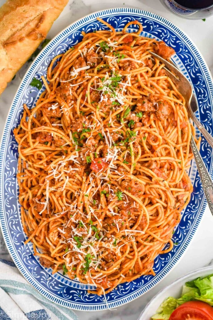 Overhead view of a platter of one pot Sausage Spaghetti with two forks for serving. Bread and bowl of salad beside
