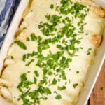 over head view of a baking dish with blue handles on a wood board holding sour cream chicken enchiladas, with a white sauce, garnished with a lot of cilantro - 13