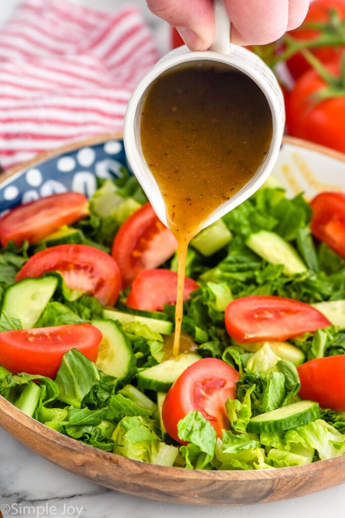 man's hand pouring simple vinaigrette onto a greens salad with tomato slices and cucumber slices