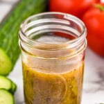 Jar of simple vinaigrette. Cucumber and tomatoes sitting in background