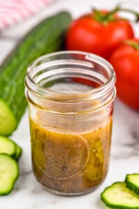 Jar of simple vinaigrette. Cucumber and tomatoes sitting in background