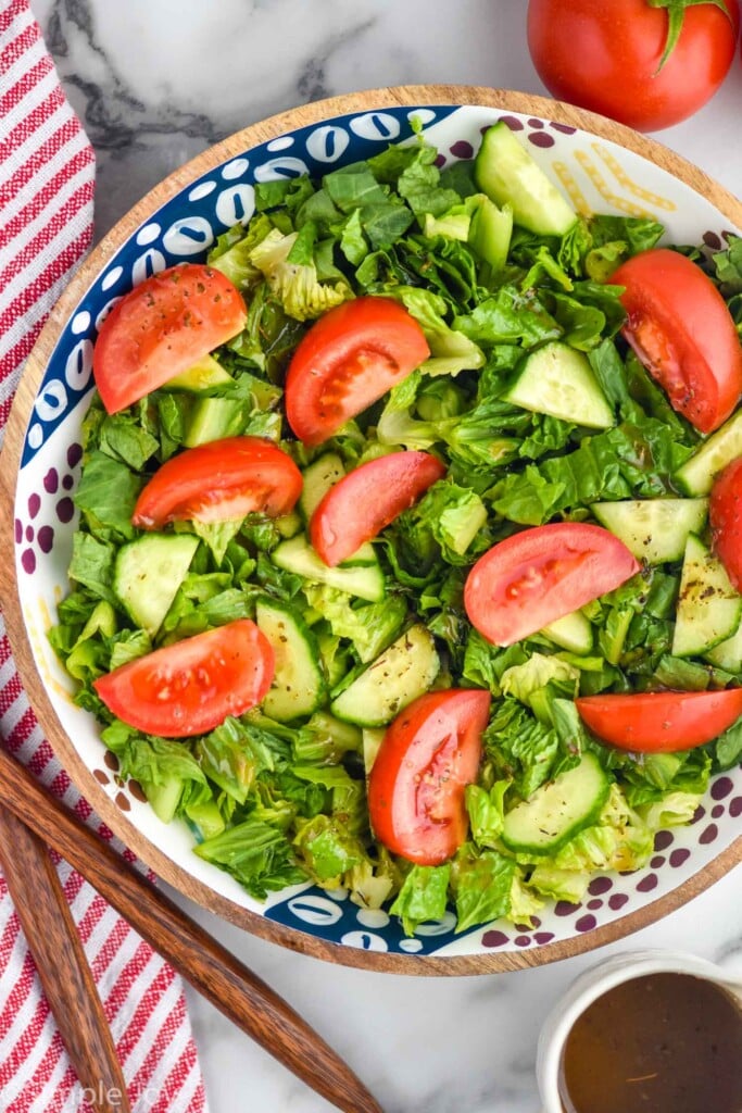 overhead of salad topped with tomato slices and sliced cucumber. Jar of simple vinaigrette sitting beside