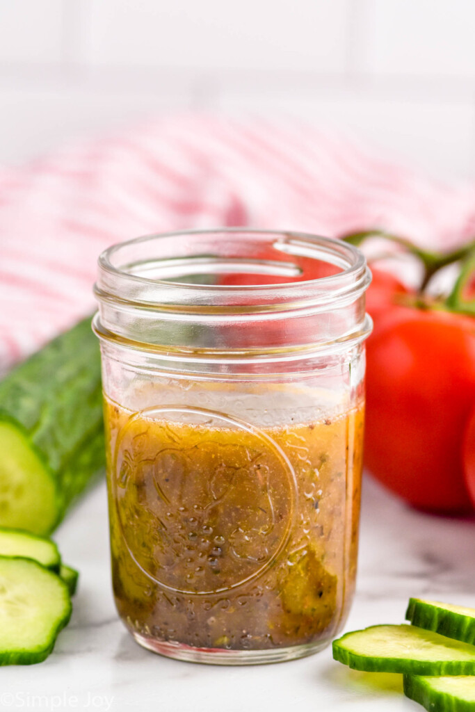jar of simple vinaigrette with cucumber and tomatoes sitting in background