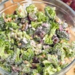 Overhead view of Broccoli Salad in a glass bowl with wooden spoon and grapes beside. - 9