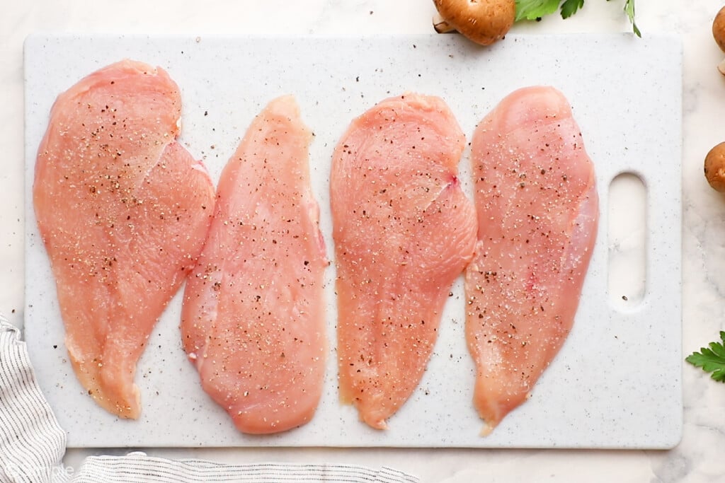 overhead of seasoned chicken cutlets on a cutting board