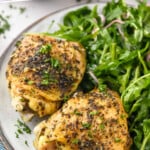Pinterest graphic for Crock Pot Chicken Thighs recipe. Text says, "slow cooker chicken thighs simplejoy.com." Image shows a plate with Crock Pot Chicken Thighs and arugula salad.