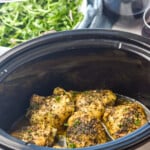 Pinterest graphic for Crock Pot Chicken Thighs recipe. Text says, "slow cooker chicken thighs simplejoy.com." Image shows a crock pot with Crock Pot Chicken Thighs recipe in it. Glasses of red wine and salad beside.