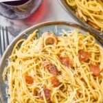 Pinterest graphic for pasta carbonara recipe. Image shows Plate of Pasta Carbonara garnished with parmesan cheese. Forks, glass of red wine, and bread beside. Text says, "the best carbonara recipe simplejoy.com"