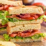 Side view of BLT sandwich cut in half and stacked on top of each other on a wooden board. Chips beside. - 9