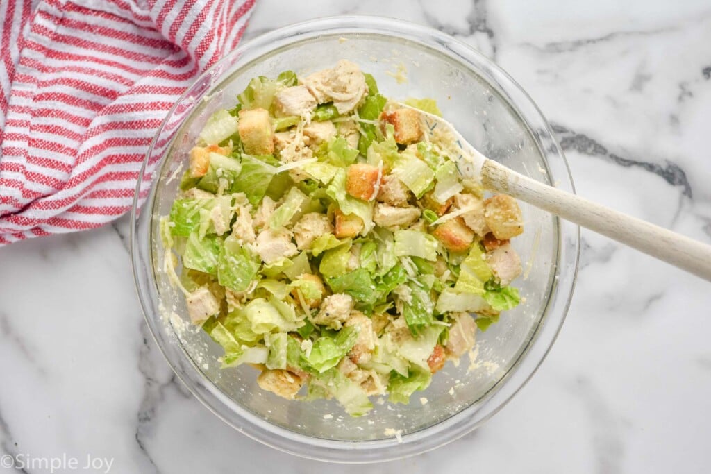 Overhead view of a glass mixing bowl of Chicken Caesar Wrap filling after being mixed with a spatula.