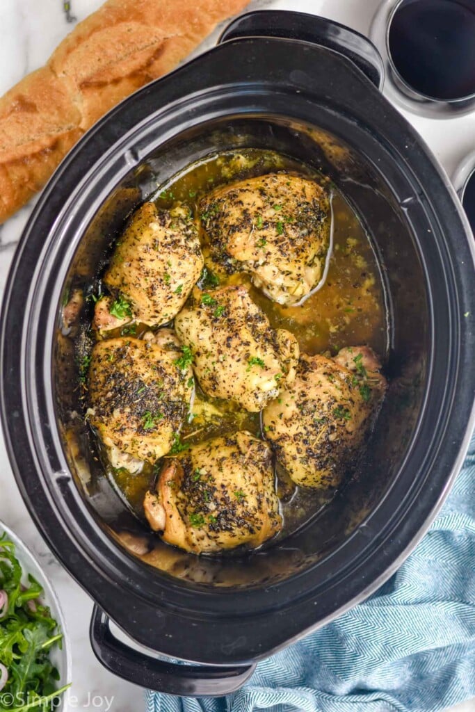 Overhead view of crock pot with Crock Pot Chicken Thighs. Bowl of salad, glass of red wine, and bread beside.