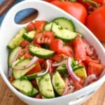 Bowl of Cucumber Tomato Salad sitting on a cutting board. Fresh tomatoes sitting in background - 19